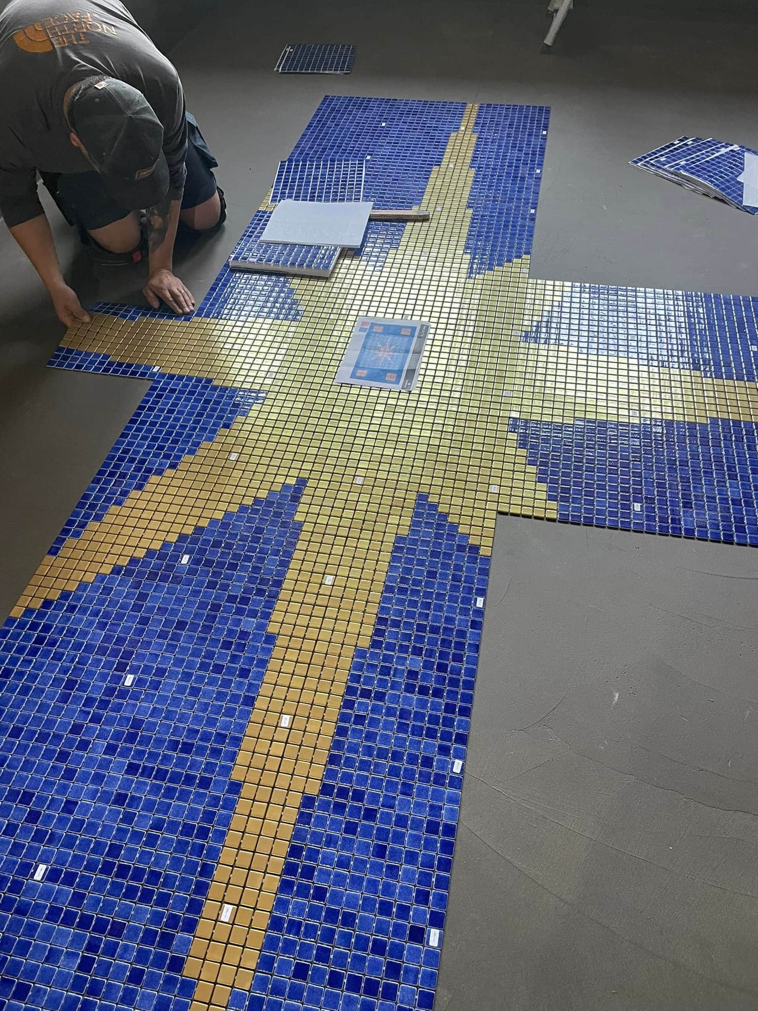 Plattsättare som arbetar med att lägga mosaik i botten av en pool.