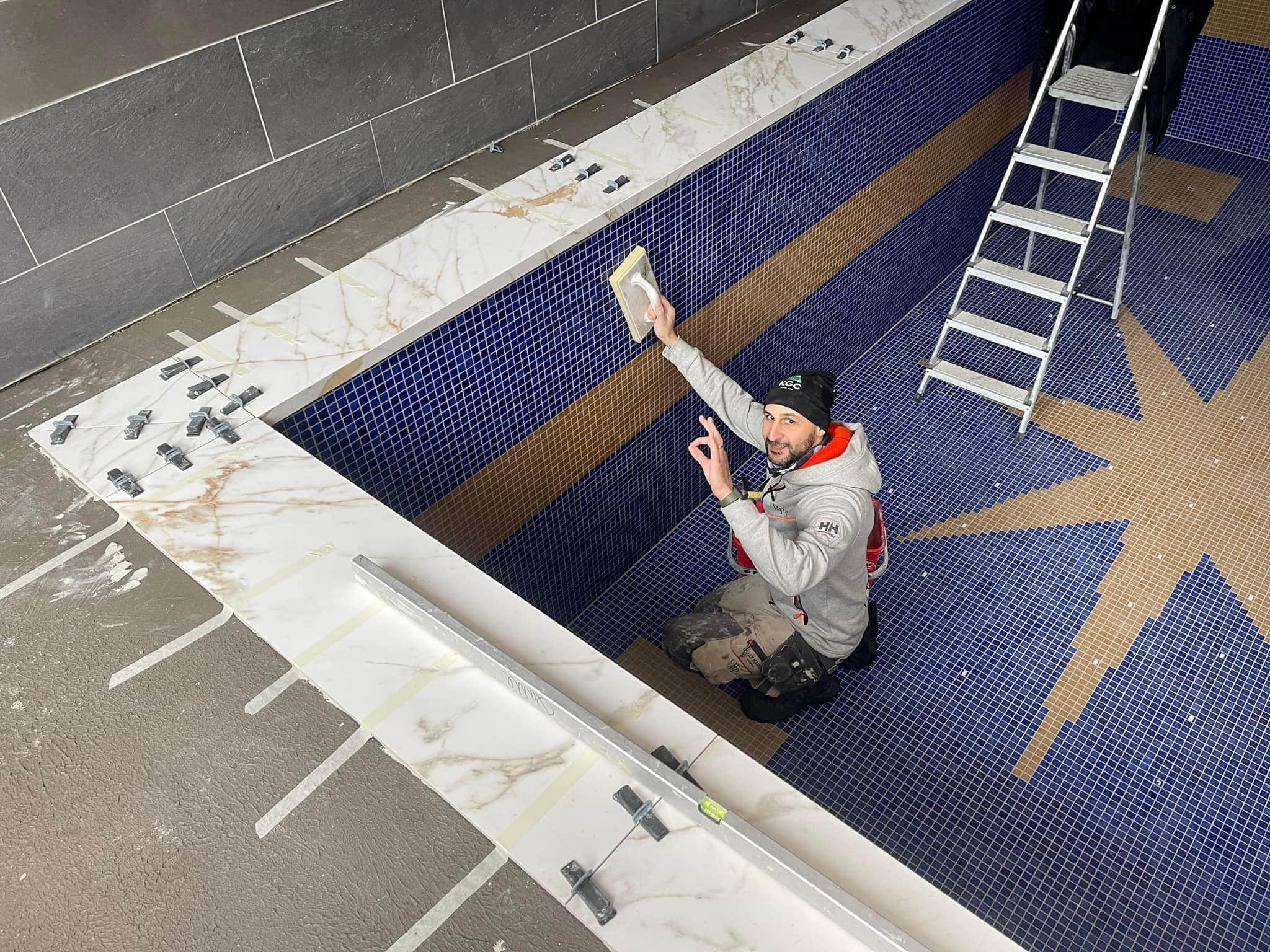 Plattsättare i arbete med att foga kaklet i en inomhuspool.